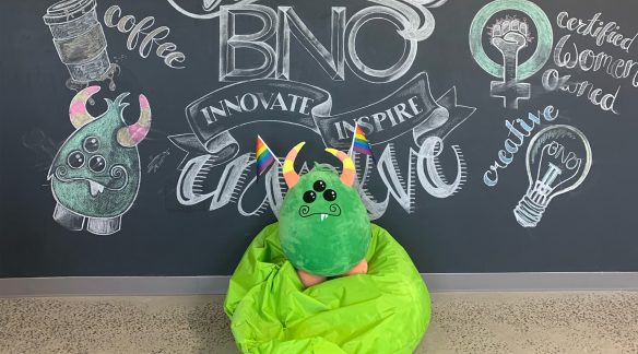 The 3i monster holding Pride flags on a bean bag chair.